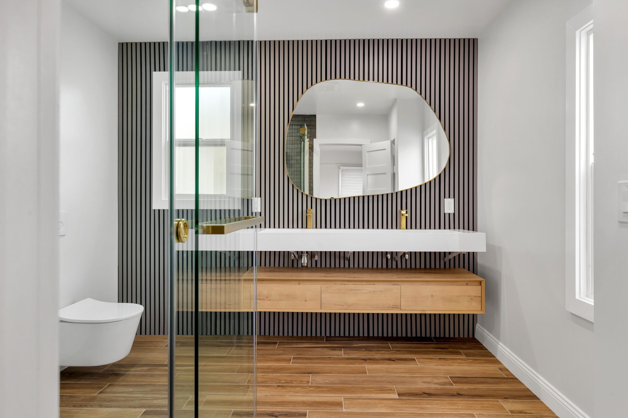 San Francisco bathroom remodel with a floating wood vanity, wall-hung toilet, slatted accent wall and organic-shape mirror, built by WDC