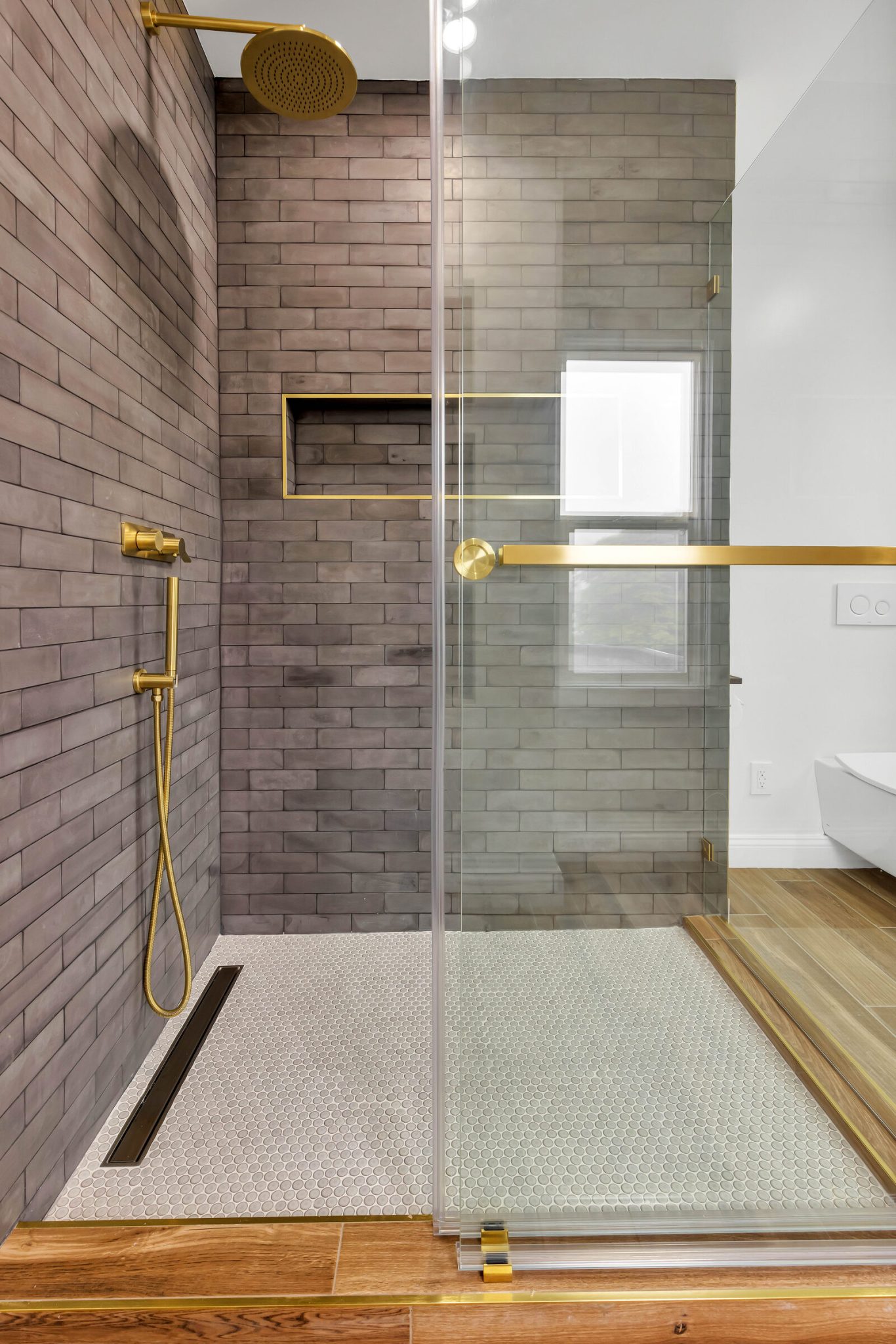 Walk-in shower in a San Francisco bathroom remodel with a linear drain, penny tile floor, gray brick-look wall tile and brushed gold fixtures