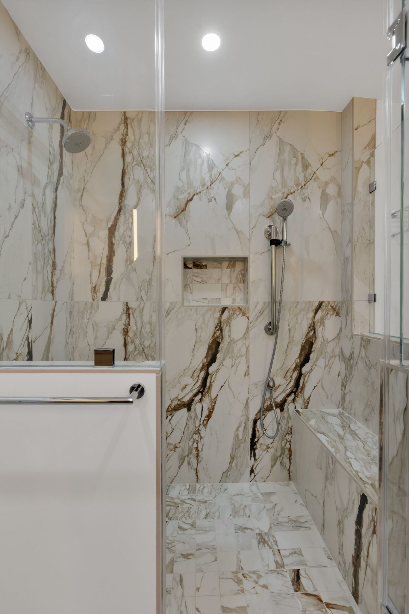 Large-format veined stone shower in a San Francisco bathroom remodel by WDC, with a recessed niche, a bench and a slide-bar hand shower
