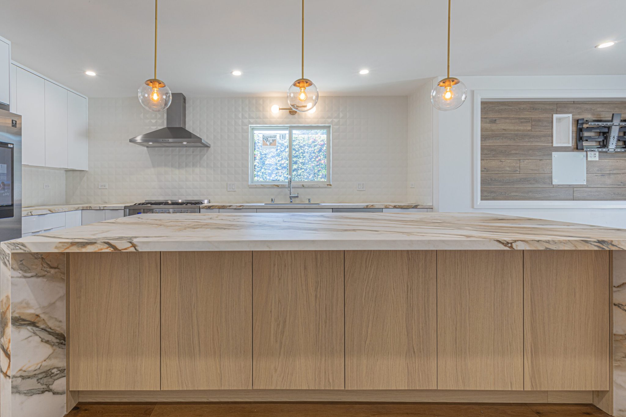 San Francisco kitchen remodel with a white island, veined stone counters, glass pendant lights and a stainless range under a chimney hood